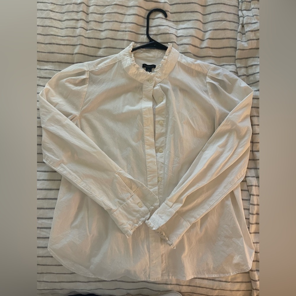 White cotton button-up shirt with ruffle details on the cuffs and collar.